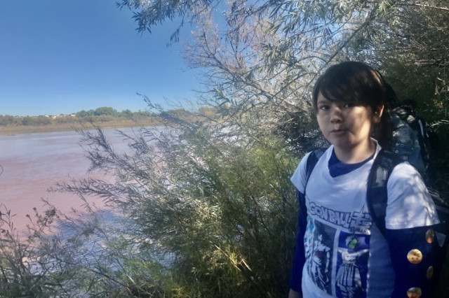 Young adult wearing t-shirt and backpack with muddy water in the background