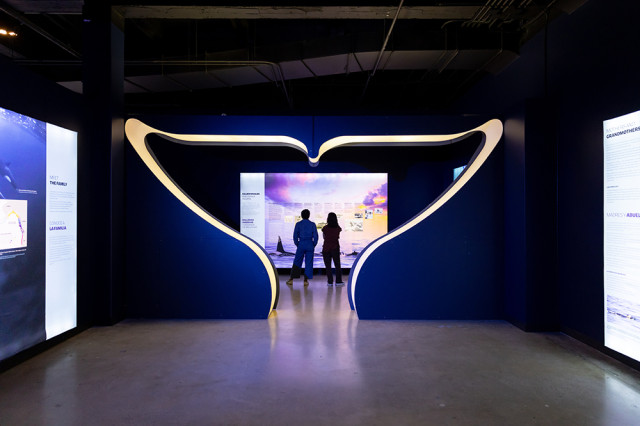 Two visitors in the distance beyond a cut-out of a whale's tale fin