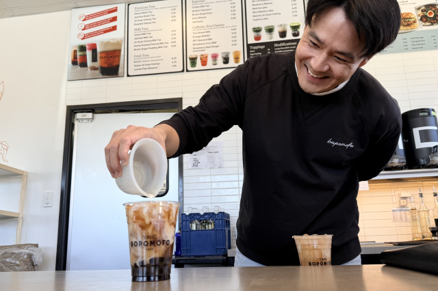 Philip Wang carefully examining the visually striking, three-tiered layers—bright pink, solid white, and dark green—of the Ba-La Matcha in a clear plastic cup