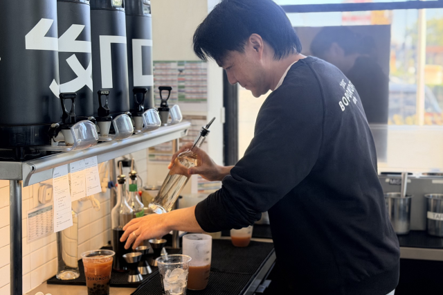 A close-up of Philip Wang pouring a vibrant pink layer of fresh guava juice into the base of a clear Bopomofo Cafe cup.