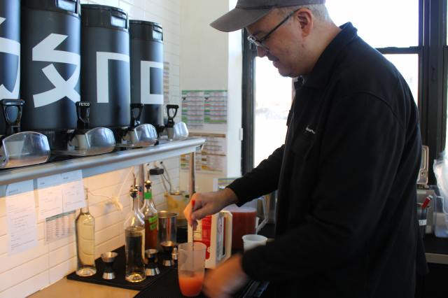 Eric Wang preparing the Carrot Matcha Latte, highlighting the drink's bright, unconventional orange hue from the fresh carrot juice at the bottom of the cup.