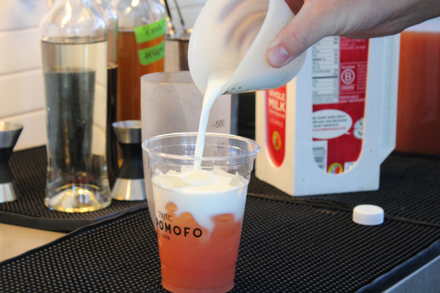 Eric Wang preparing the Carrot Matcha Latte, highlighting the drink's bright, unconventional orange hue from the fresh carrot juice at the bottom of the cup.