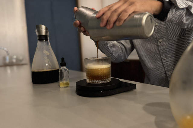 Barista using a shaker to pour espresso into a glass of artisanal coffee.