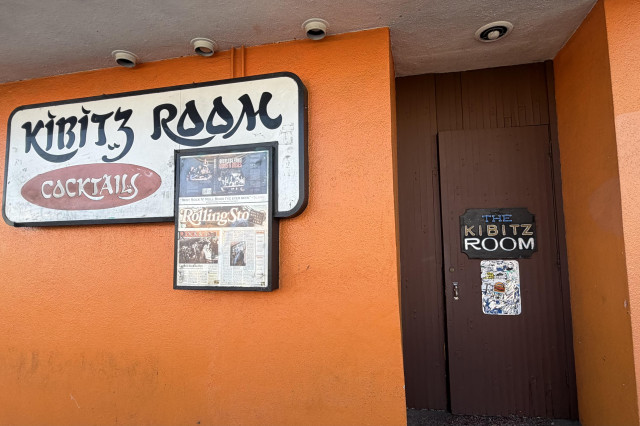 Orange building with a brown door next to a sign that reads "Kibbitz Room".