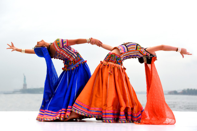 Dancers in blue and orange skirts and colorful tops, holding hands while bending backwards away from one another