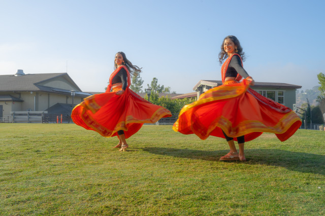 Two dancers on a green lawn, swirling in orange skirts and black tops