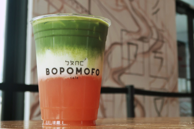 Bright colored drink with layers of green, white, and orange on wood table top