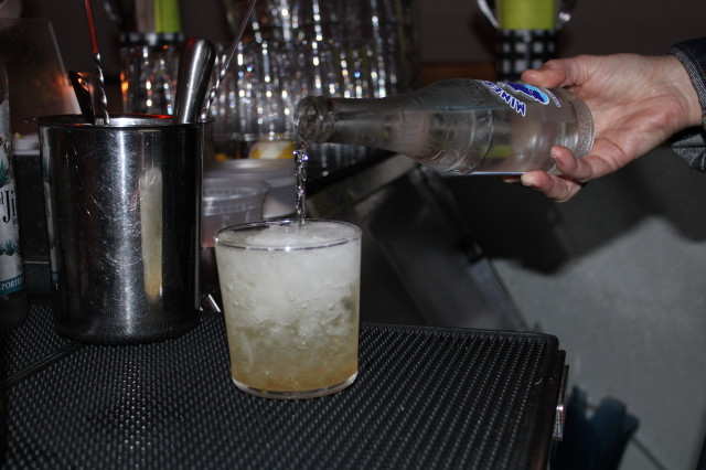 Close-up of person pouring mineral water into a cocktail in a chilled highball glass.