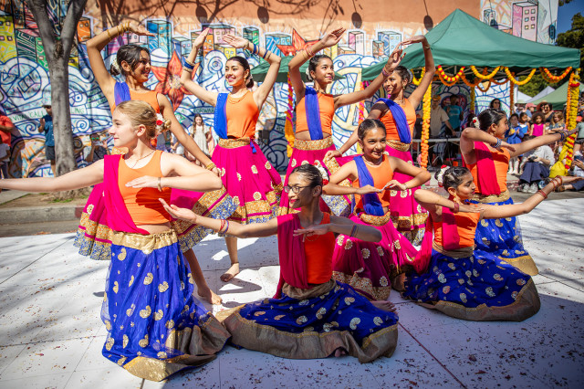 Young women and girls in orange tops and pink and blue skirts, posing with arms raised to the side