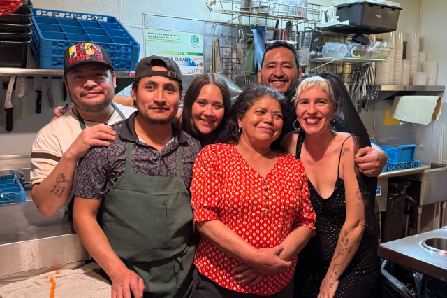 A group photograph of The Ruby Fruit founders and staff members standing together in the restaurant. From left to right: Froilan, Mario, Mara, Regina, Oswaldo, and Emily.