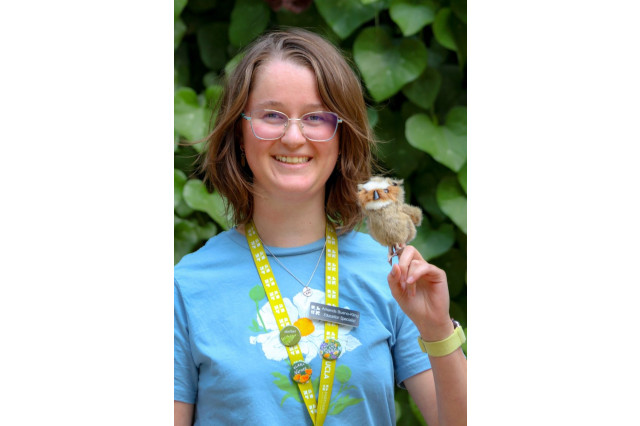 Chantal Ochoa-Clark, wearing sunglasses and holding a stuffed-animal bird on her finder, against a background of green leaves