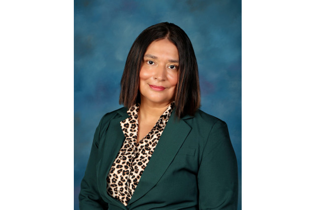 Head and shoulders portrait of Linda Banuelos, wearing a leopard print blouse and blazer, against a blue background