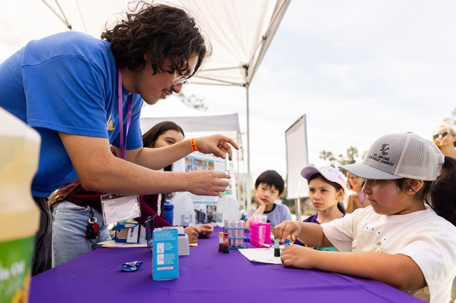 Young adult holding up a test tube towards children across a table