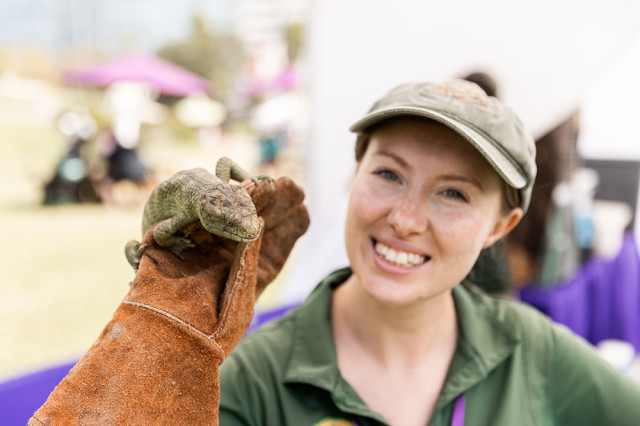 Woman smiling and holding a lizard on a gloved hand