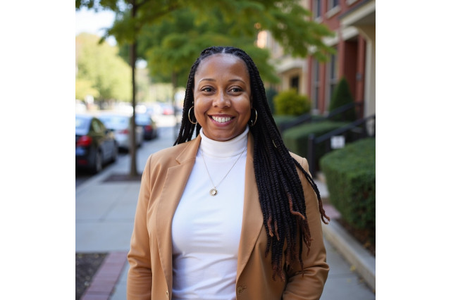 DeAnna Lee Rivers, wearing a white turtleneck and tan blazer, standing outside on the sidewalk of a neighborhood street