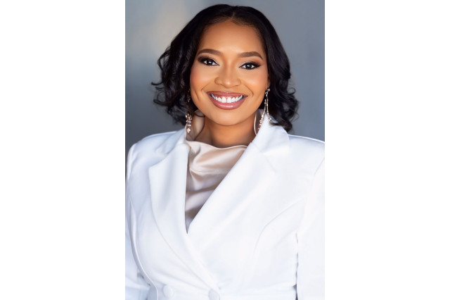 Head and shoulders portrait of Fre'Drisha Dixon, wearing a white jacket, smiling, and looking into the camera