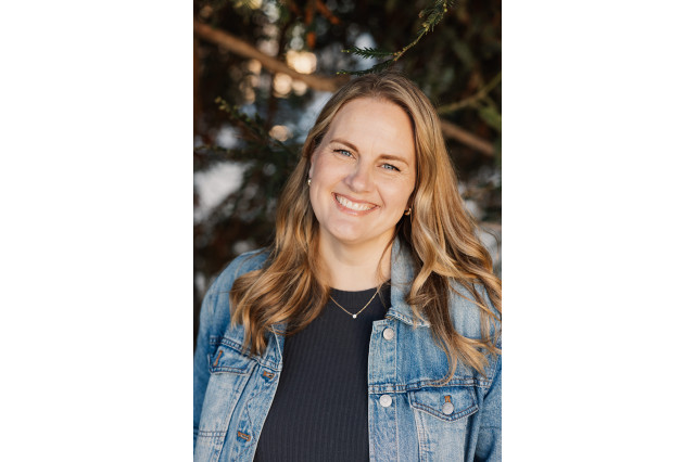 Head and shoulders portrait of Jill Arbini, smiling and wearing a blue jean jacket over a black t-shirt