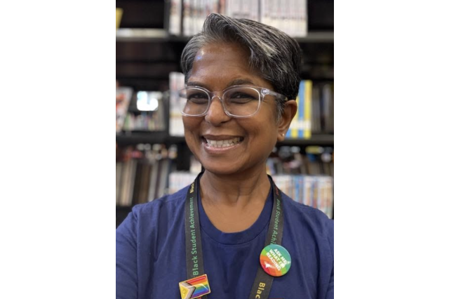 head and shoulders portrait of Kirti Baranwal, wearing glasses and smiling, with bookshelves behind her