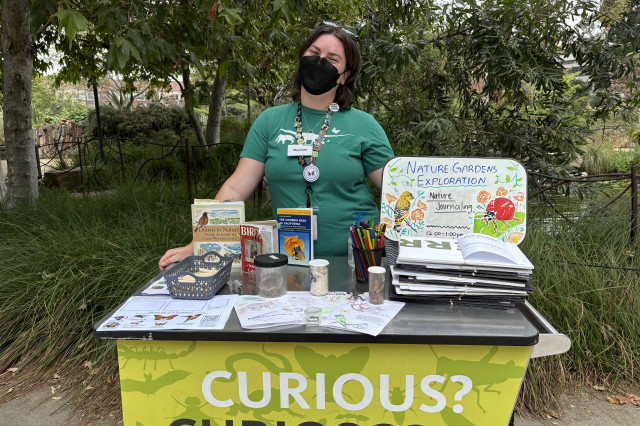 Shannon Subers weating a mask and standing behind a cart with a display educational materials 