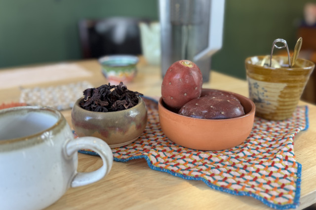 Tea cup and small dishes of fresh tea-making ingredients set on a placemat, on a wooden counter.