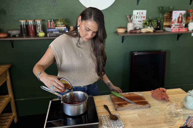 Woman pouring maple syrup into a boiling pot of tea on the stove.