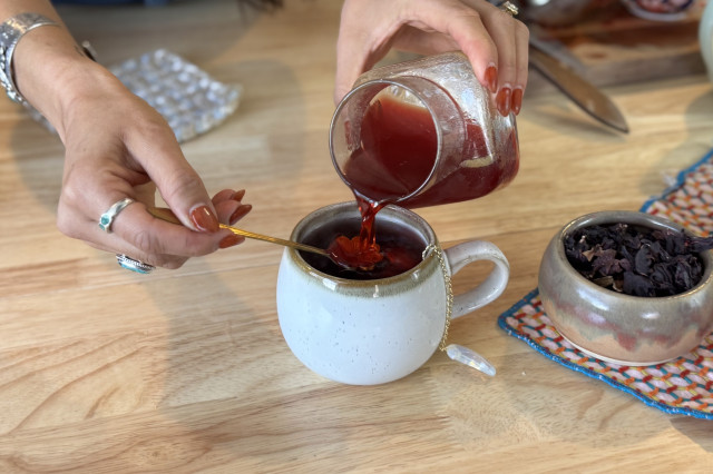 Woman pouring red syrup into a white tea cup of brewed tea.
