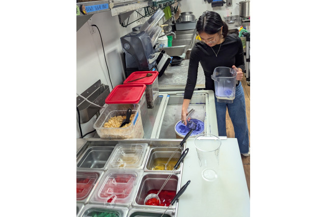 Young woman scooping ube ice cream into a blender next to a counter full of mix-ins.