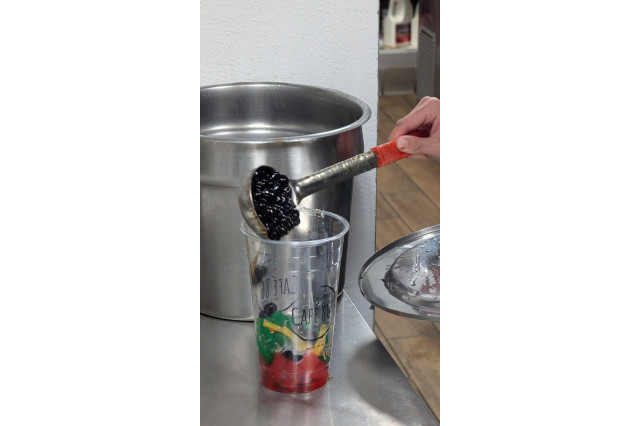 Tapioca pearls being poured into a glass of fruit jellies to make halo-halo.