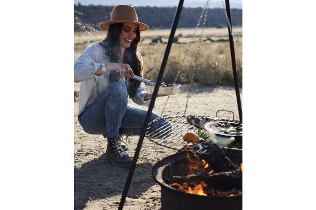 Woman kneeling next to an outdoor grill, cooking over the fire.