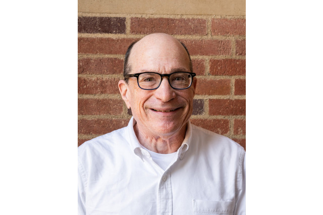 Head and shoulders portrait of David Saltzberg, wearing glass and a white button down shirt, against a brick wall