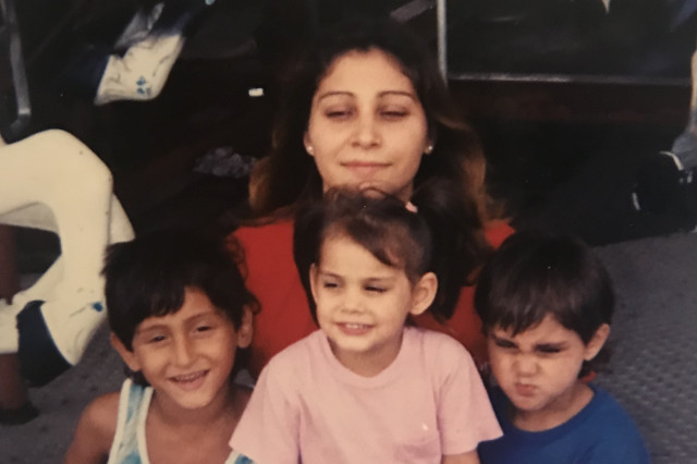 Young mother sitting with three young kids in her lap, two boys on either side of a young girl.