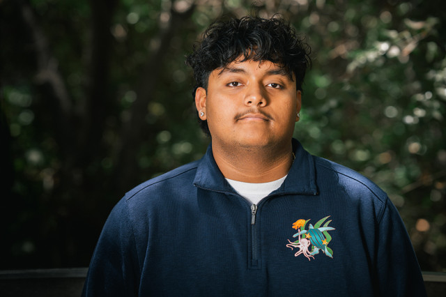 Head and shoulders portrait of Adrian Alvarado , against a leafy green background