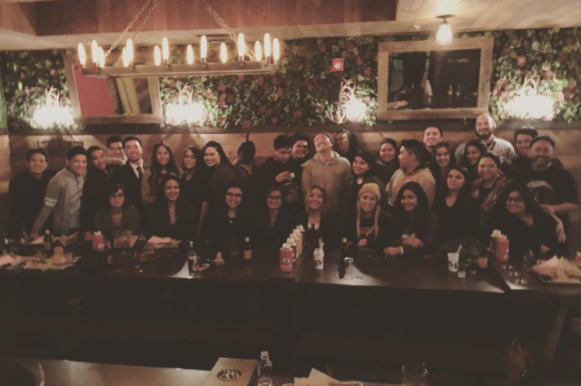 32 men and women standing together behind a long table at a restaurant, smiling and posing for a staff photo.