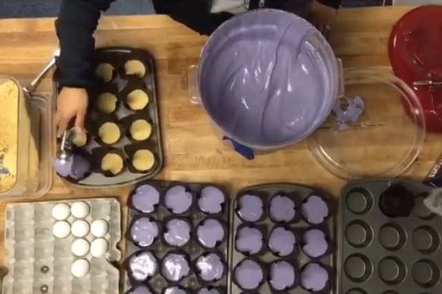 Counter top covered in muffin trays filled with purple ube batter.