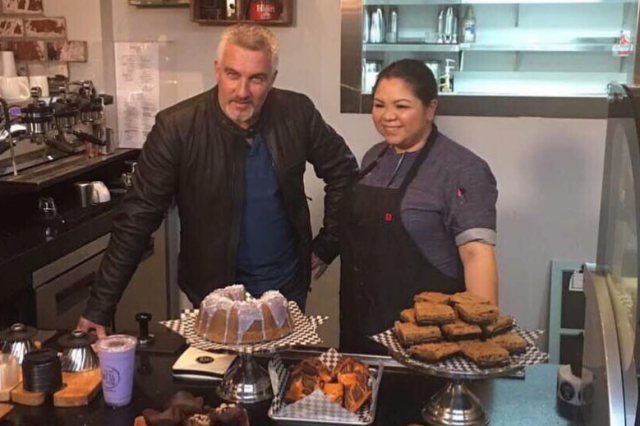Chef Ginger standing in an apron next to a Food Network interviewer, behind a counter full of her pastries.