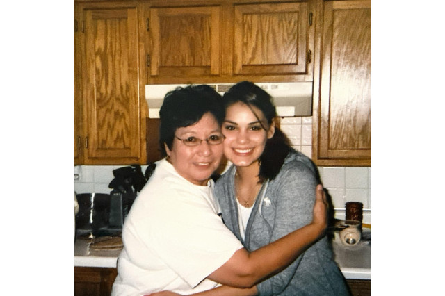 Young woman giving her grandmother a side hug in a kitchen with wooden cabinets. 