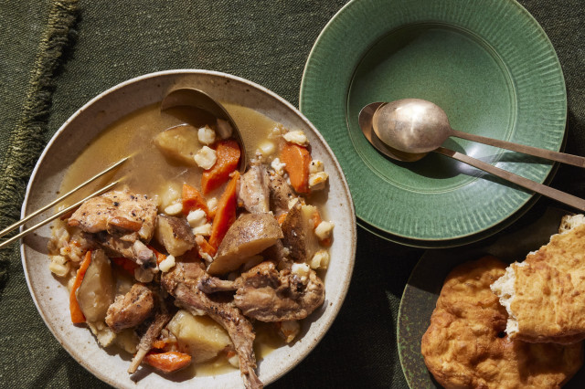 Bowl of meet stew with vegetables next to a plate of fry bread and an empty bowl and spoon.