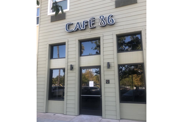 Beige storefront with three tall windows and a glass door underneath a sign that says "Cafe 86".