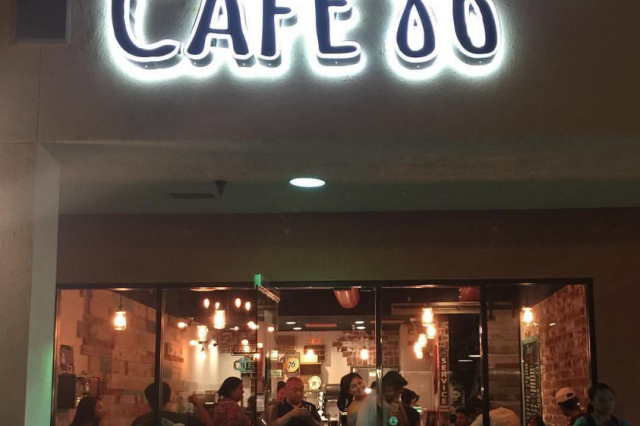 Cafe store front at night with people visible inside the glass walls, below a bright lit "Cafe 86" sign.
