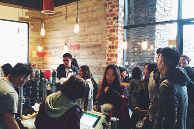 Cafe entrance crowded with customers surrounded by unfished wood walls and bright glass windows.
