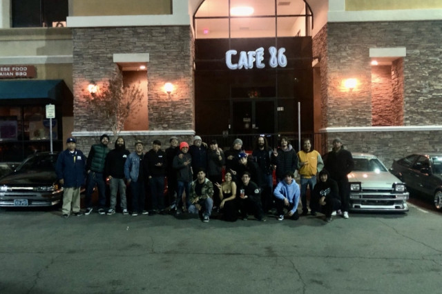 Car meet at night in front of a brightly lit cafe.