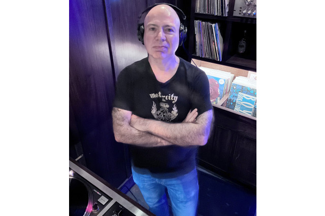 Mike Cimicata aka mikecmusic, wearing headphones, with arms crossed, standing in front of shelves of vinyl records