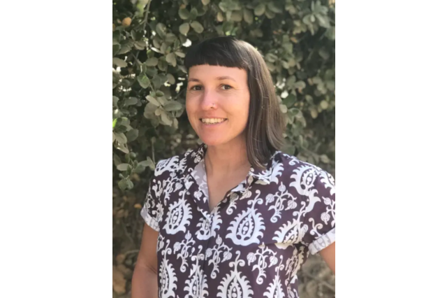 Dr. Rachel Blakely, a white-presenting woman, stands in front of a wall of greenery. 