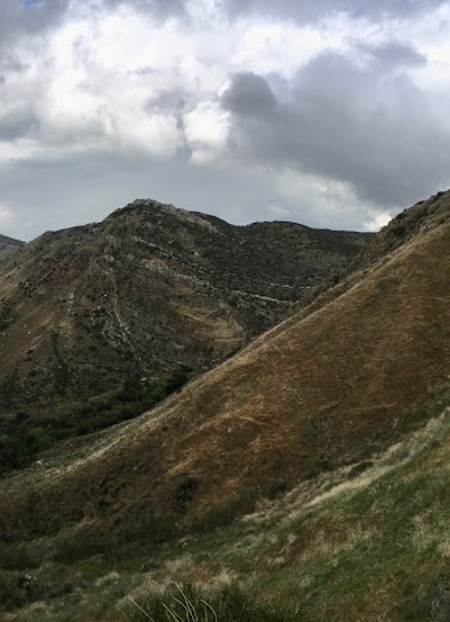 Panoramic view of hills under scenic clouds with two small hikers just visible