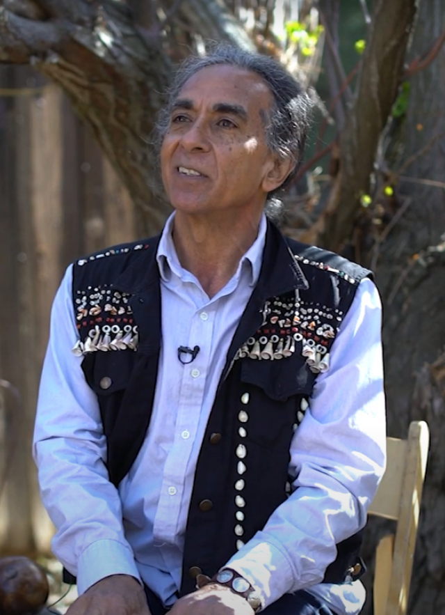 Man with white shirt and black vest. Guitar at side