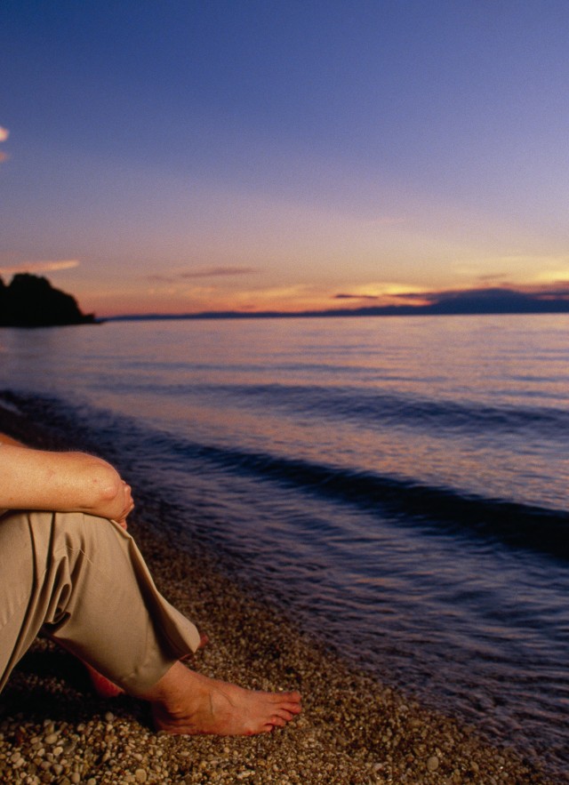 Jane Goodall sits at the waters edge on a beach staring into the horizon.