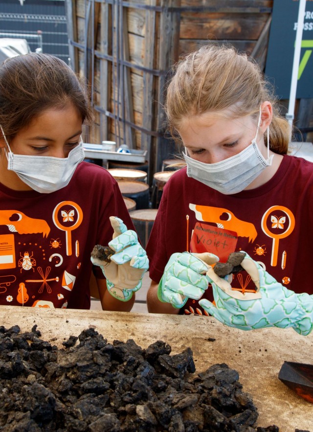 two girls wearing face masks and gloves look through fossil matrix
