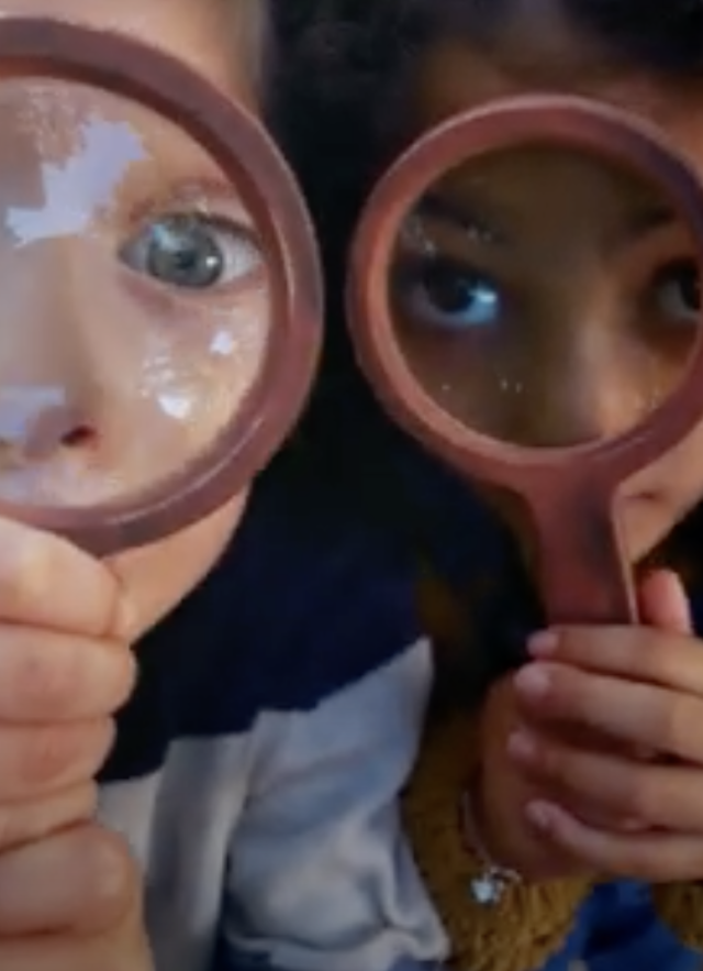 A close-up of two children holding magnifying glasses up to their face 