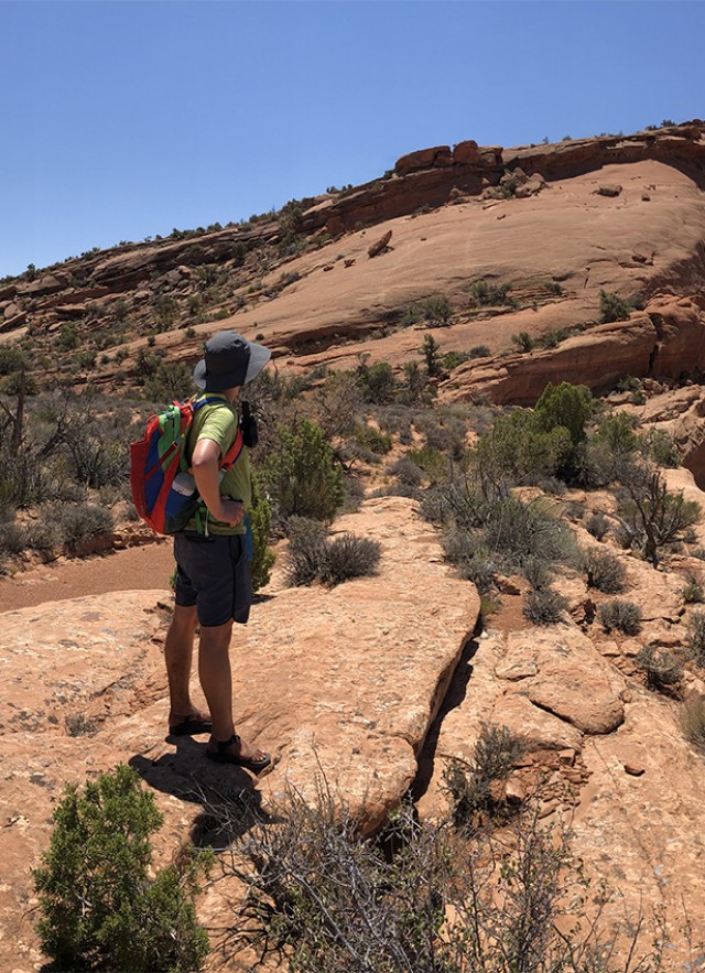 Students standing on a mountain ridge, with one looking across to the other side and the other pointing their phone at the camera