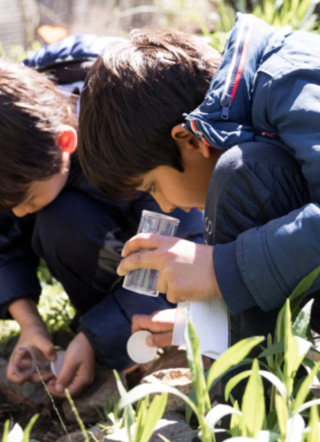 Two children crouched down together holding specimen containers in the Nature Gardens 